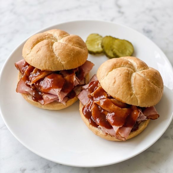 Two ham barbecue sandwiches on Kaiser rolls on a plate