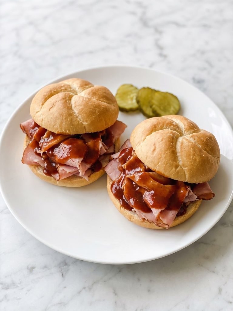 Two ham barbecue sandwiches on Kaiser rolls on a plate