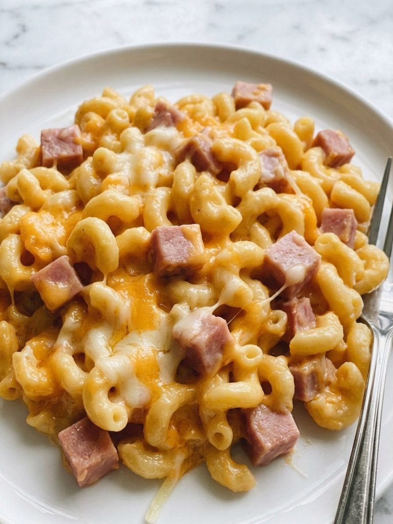A serving of ham mac and cheese casserole on a plate showing creamy macaroni and cubes of ham