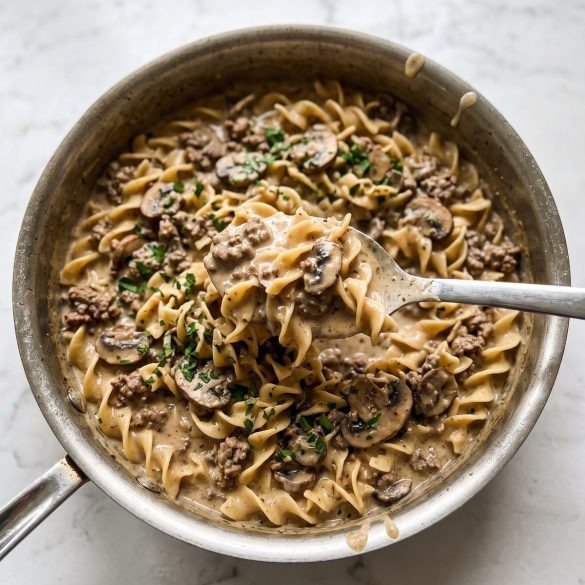 Creamy ground beef stroganoff with egg noodles and mushrooms in a skillet, with a serving scooped out