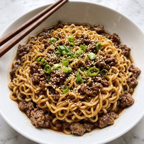 A bowl of saucy ramen noodles with browned ground beef and green onions