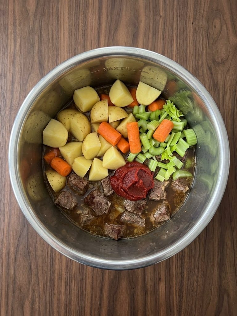 Step 5: raw Yukon Gold potatoes, carrots and celery layered over browned beef in the Instant Pot, with tomato paste left unstirred.