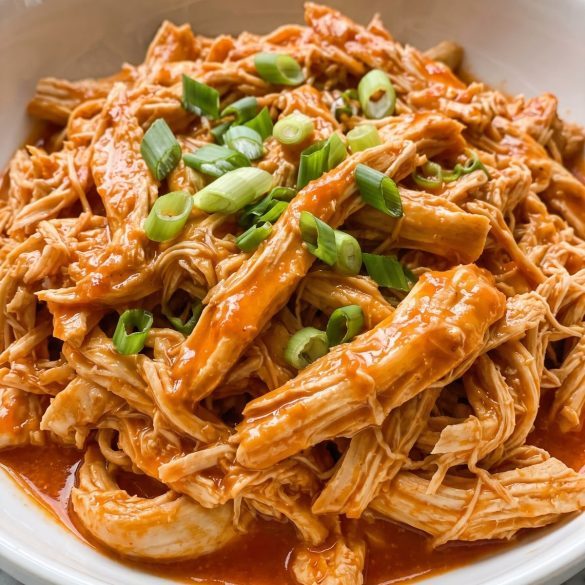 Shredded buffalo chicken in a glossy orange hot sauce in a bowl