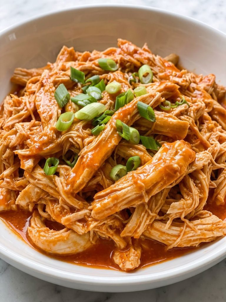 Shredded buffalo chicken in a glossy orange hot sauce in a bowl