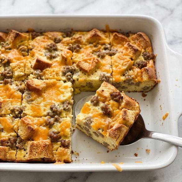 Sausage, egg and cheese bread casserole in a white baking dish with one square lifted out