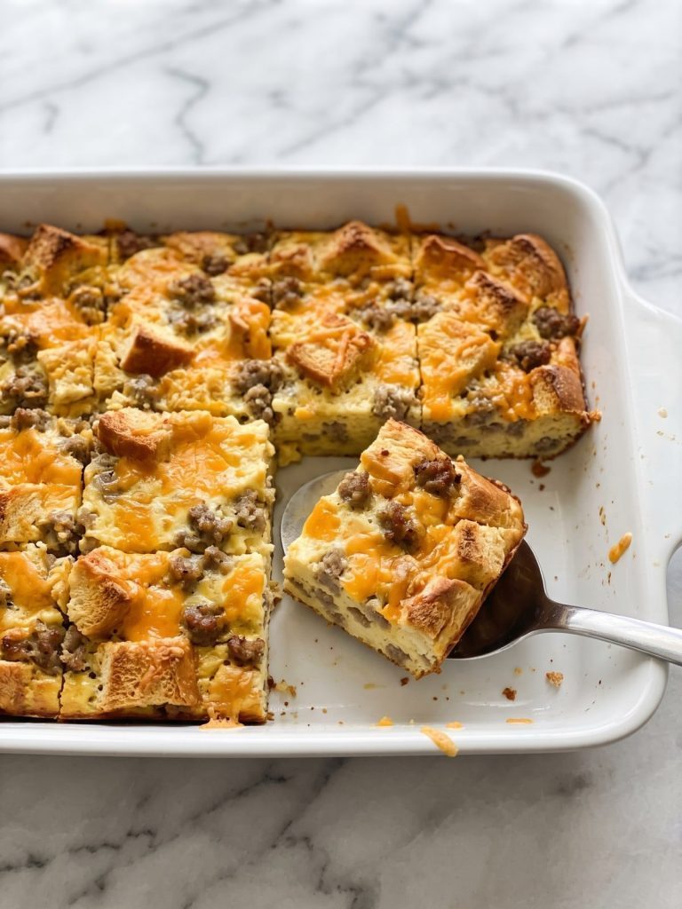 Sausage, egg and cheese bread casserole in a white baking dish with one square lifted out