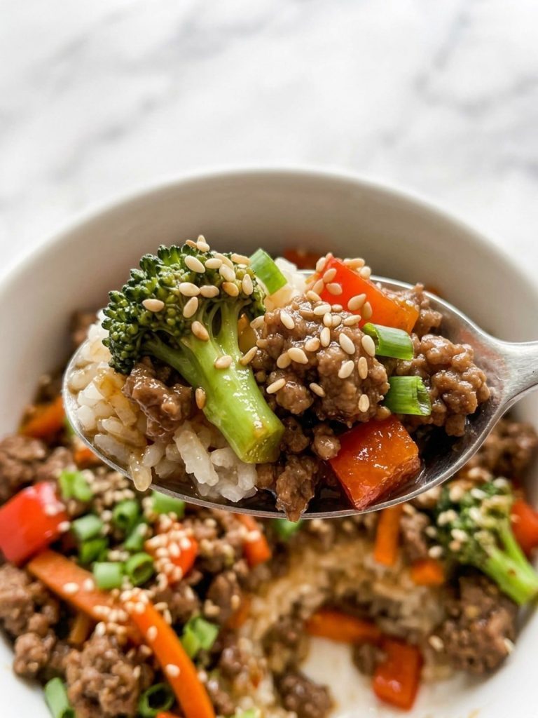 Close view of a spoonful of browned ground beef, broccoli and red pepper in a glossy soy sauce over rice