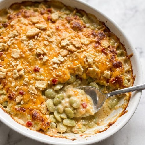 A casserole dish of cheesy lima bean casserole with a golden cracker topping and a spoonful scooped out
