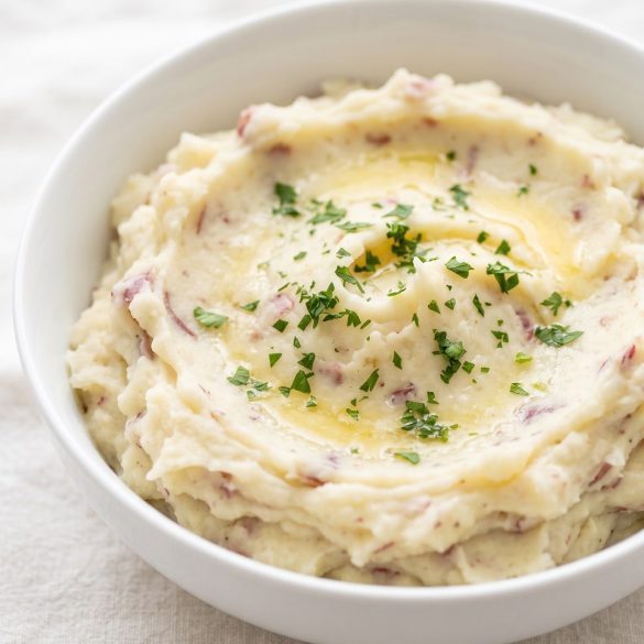 A bowl of skin-on mashed red potatoes with melted butter and parsley