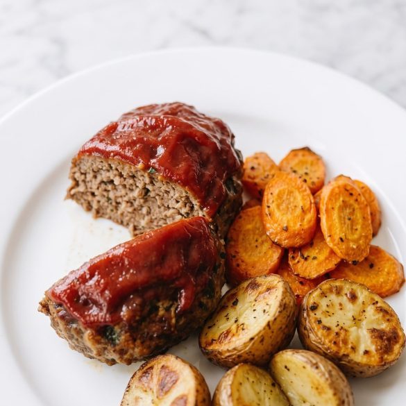 A glazed mini meatloaf with roasted carrots and baby potatoes on a plate