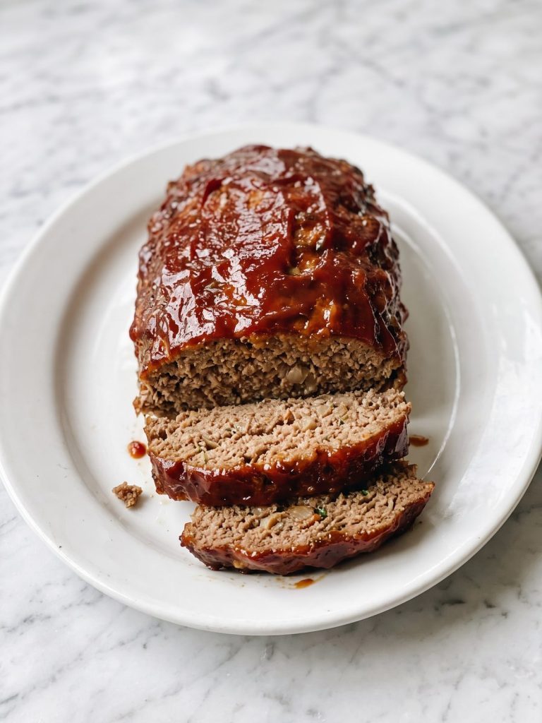 A baked meatloaf with a glossy caramelized ketchup and brown sugar glaze, two slices cut