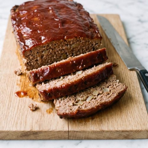 Sliced meatloaf with a glossy red tomato sauce topping on a wooden board