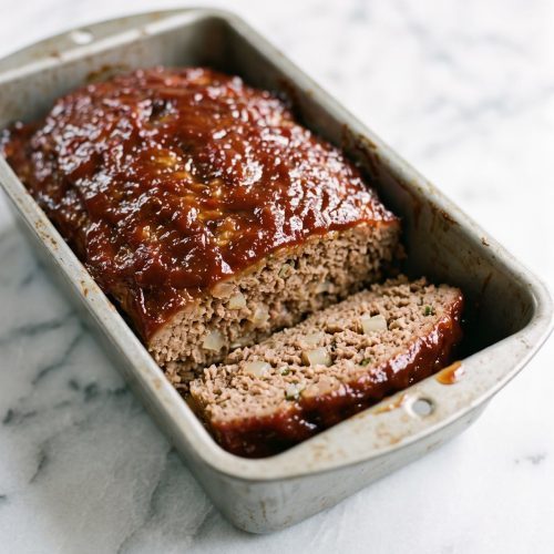 Glazed meatloaf in a loaf pan with a slice cut to show the inside.