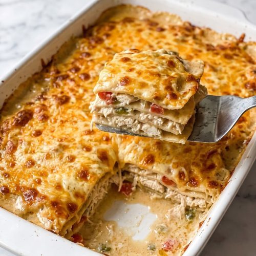 Baked Mexican chicken casserole in a white dish with bubbling cheddar and one square lifted out to show the corn tortilla layers