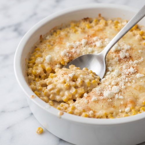 Creamy Mexican street corn casserole scooped from a casserole dish, showing corn kernels and cotija topping.