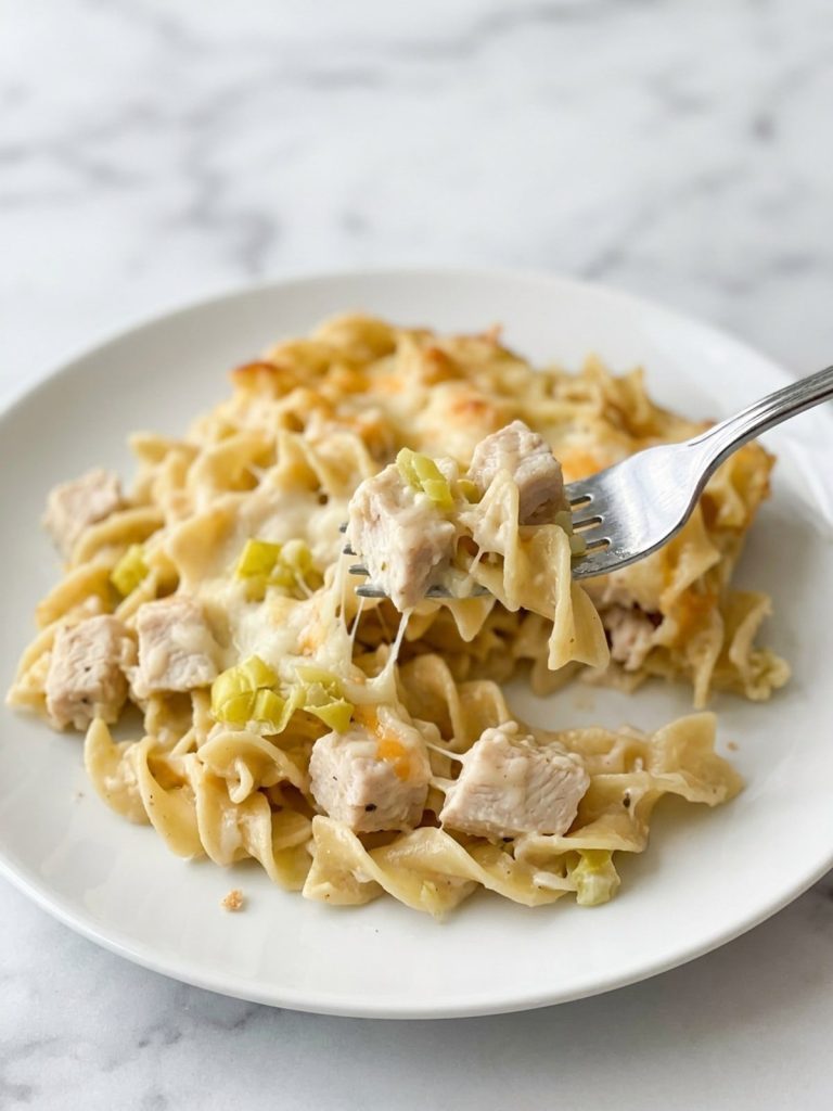 Close view of a serving of creamy chicken noodle casserole with pepperoncini and melted cheese on a fork