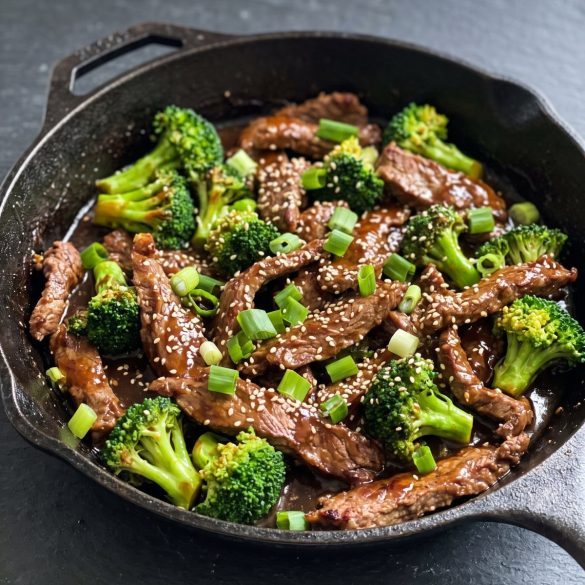A skillet of crispy Mongolian beef strips and broccoli florets in a glossy brown hoisin sauce with scallions and sesame seeds
