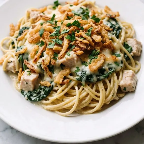 A serving of creamy chicken spinach spaghetti casserole with melted Monterey Jack and crispy fried onions on a plate