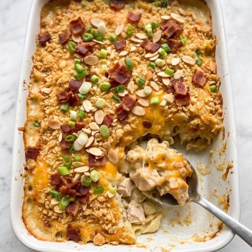 A 9x13 dish of Neiman Marcus chicken casserole with a golden cracker crust, bacon and green onions, a serving scooped out