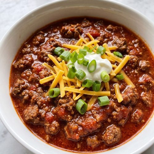 A bowl of thick no bean chili topped with cheddar, sour cream and scallions
