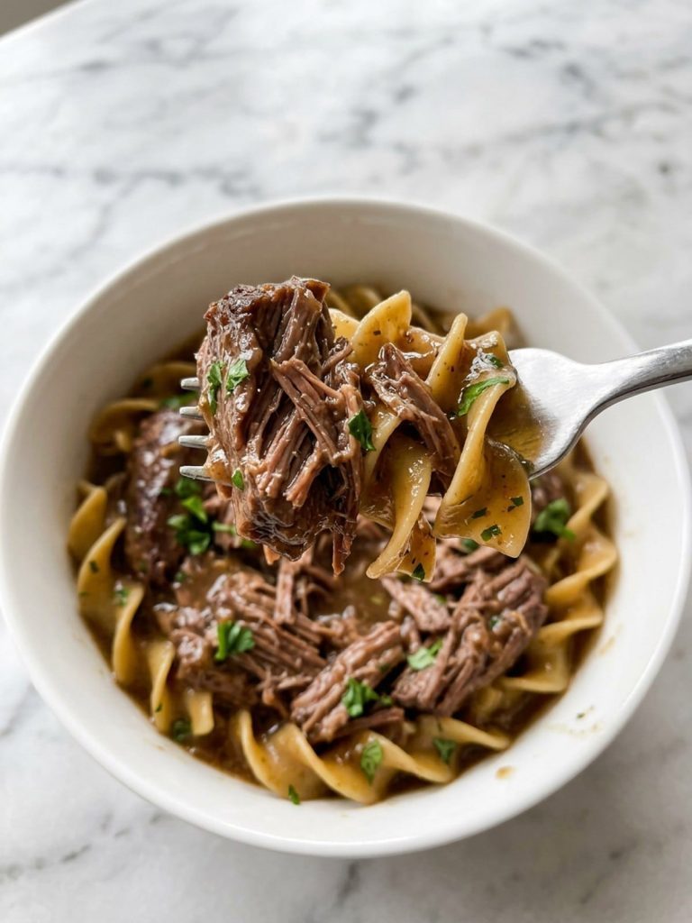 Close view of a forkful of fork-tender beef and egg noodles coated in brown gravy