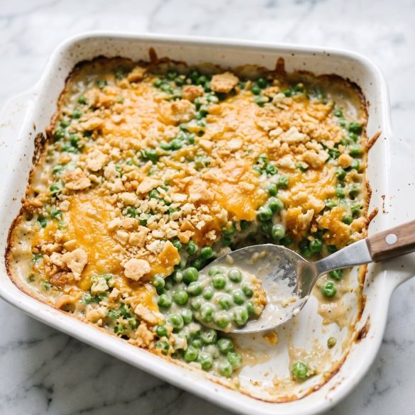 A square baking dish of green pea casserole with a golden cracker crumb topping, one corner scooped out to show the creamy peas