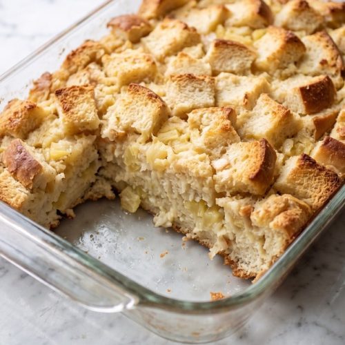 Golden pineapple and bread casserole with a portion scooped out to show the soft center