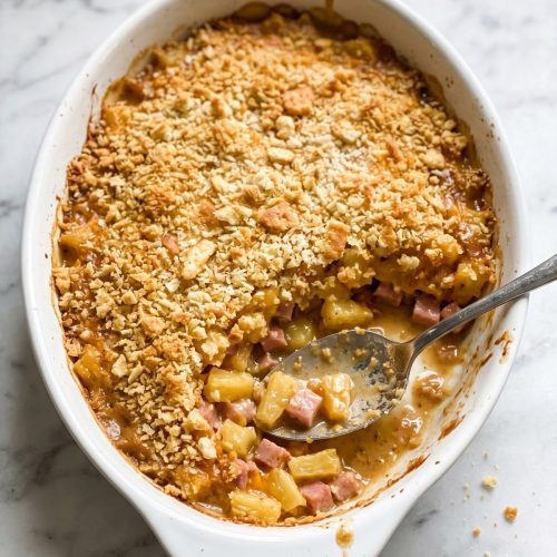 A casserole dish of pineapple and ham casserole with a golden Ritz cracker topping, a spoonful lifted out