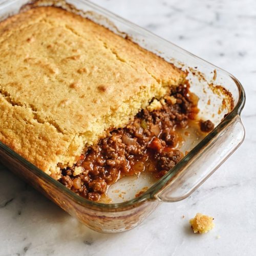 Golden cornbread casserole scooped open to show saucy ground beef underneath