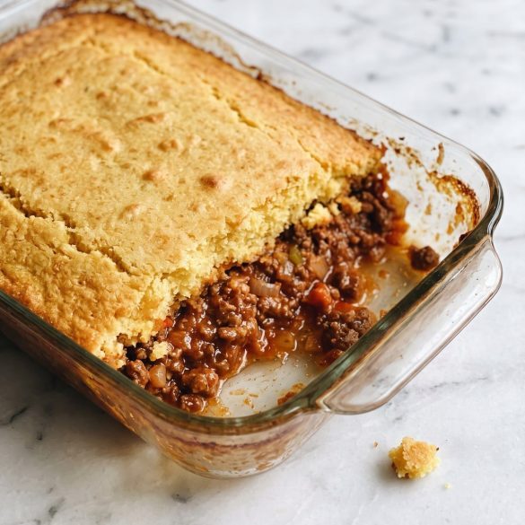 Golden cornbread casserole scooped open to show saucy ground beef underneath
