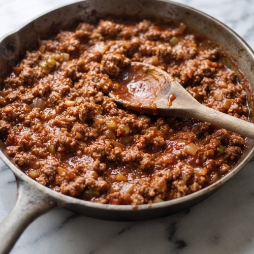 Ground-beef sloppy joe filling in a skillet with a filled hamburger bun beside it