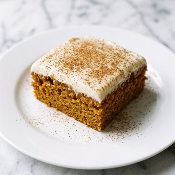 A square slice of sweet potato cake with thick cinnamon cream cheese frosting on a white plate