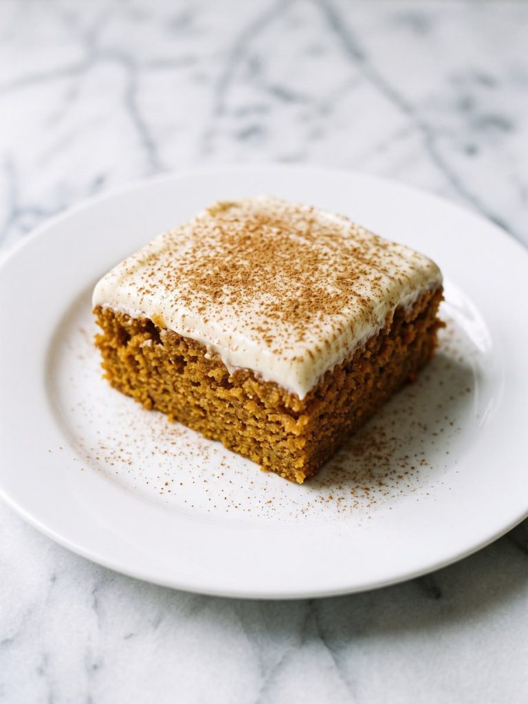 A square slice of sweet potato cake with thick cinnamon cream cheese frosting on a white plate