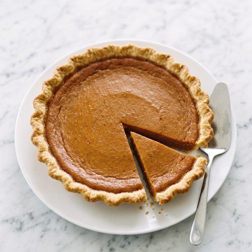 Whole Southern sweet potato pie with a slice cut out, on a white cake plate