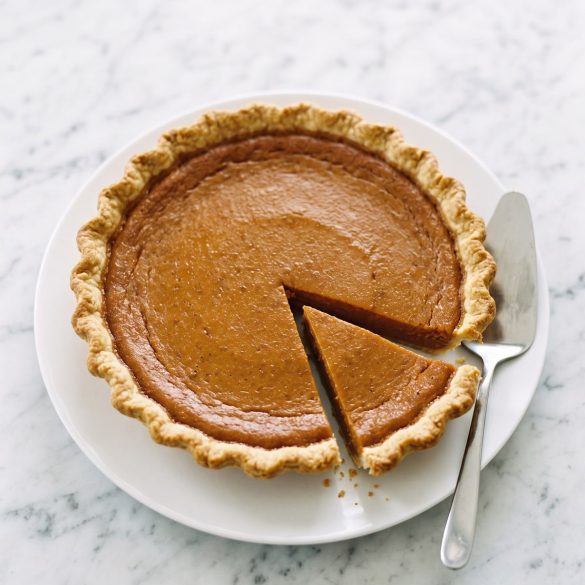 Whole Southern sweet potato pie with a slice cut out, on a white cake plate
