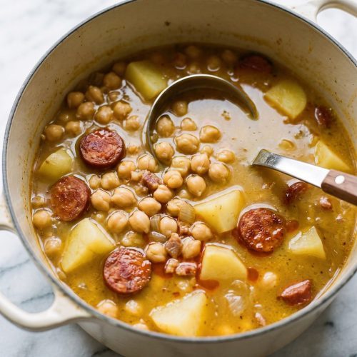 A cream Dutch oven of Spanish bean soup with garbanzo beans, potatoes and sliced chorizo