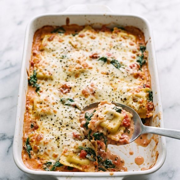 Spinach ravioli bake with bubbly golden mozzarella in a white 9x13 dish with a serving lifted out