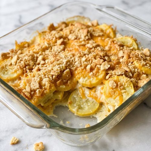 Squash casserole scooped from a baking dish, showing yellow squash and creamy filling beneath a golden cracker topping