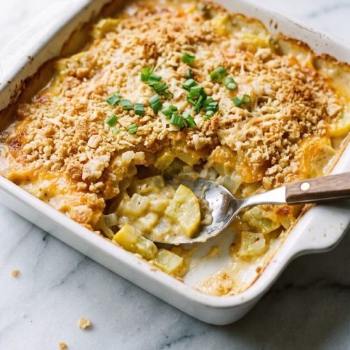 Yellow squash casserole with a golden cracker crumb topping in a square baking dish, with a serving scooped out