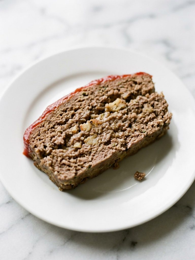 Close side view of a slice of stuffing meatloaf showing its tender center and ketchup topping
