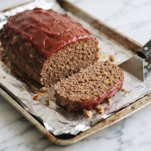 Ketchup-topped stuffing meatloaf on a foil-lined baking sheet with slices cut to show the center