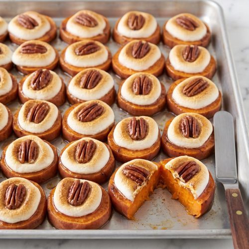 Sweet potato rounds on a sheet pan, each topped with a toasted marshmallow and a pecan half