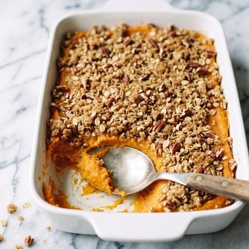 Sweet potato casserole with a golden oat and pecan crumble in a baking dish, with a serving scooped out