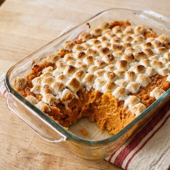 Sweet potato casserole with a scoop removed to show the creamy orange filling beneath golden mini marshmallows.