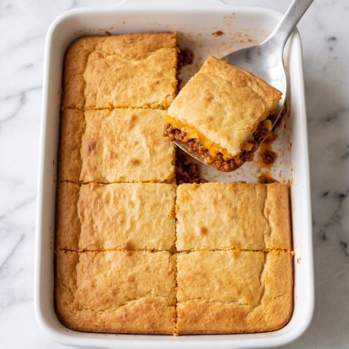 Bisquick taco bake in a white baking dish with a golden top and one square lifted out