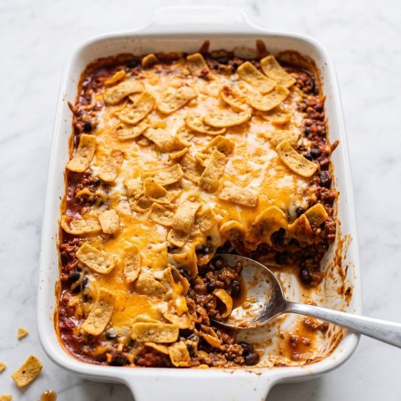 Taco casserole with Fritos in a 13x9 dish with melted cheese and crunchy corn chips on top, a serving scooped out