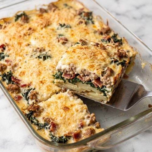 A glass baking dish of zuppa toscana casserole with a golden Parmesan top and one square served out