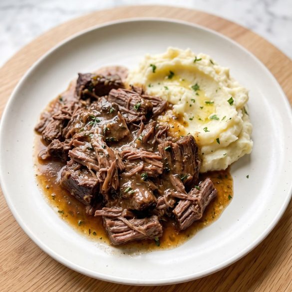 Shredded 3 packet pot roast with brown gravy over mashed potatoes on a white plate
