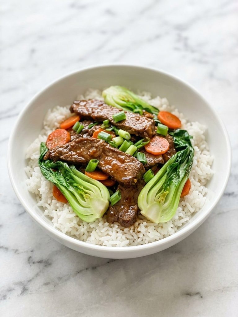 A full white bowl of beef and bok choy stir fry over steamed rice