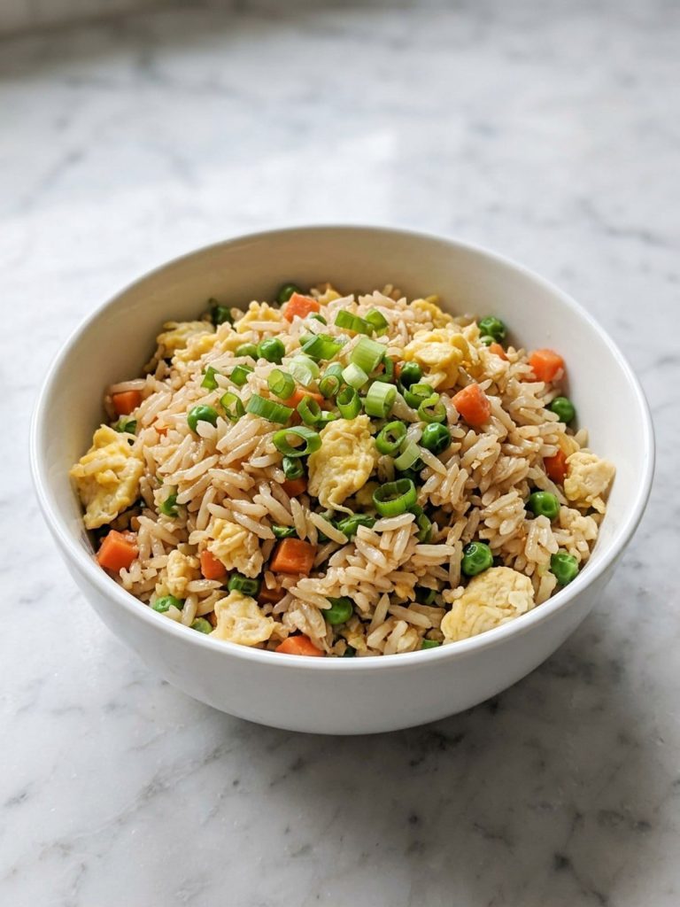 A white bowl full of fried rice with scrambled egg, peas, carrot and green onion